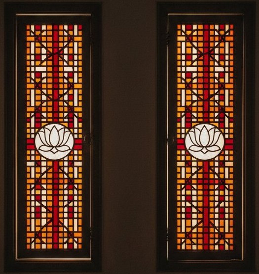 A pair of narrow pooja room door panels with lotus medallions and jaali lattice in frosted white, marigold and vermilion glass