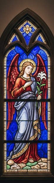Gothic arched church window section with an angel holding a lily, in cobalt, ruby and violet cathedral glass